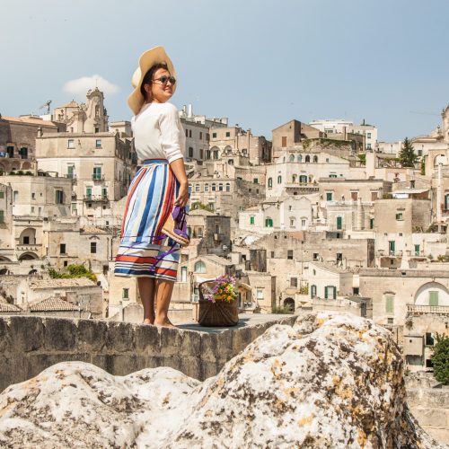 Young elegant woman tourist in historical Matera town in Italy standing on a wall looking at city landscape