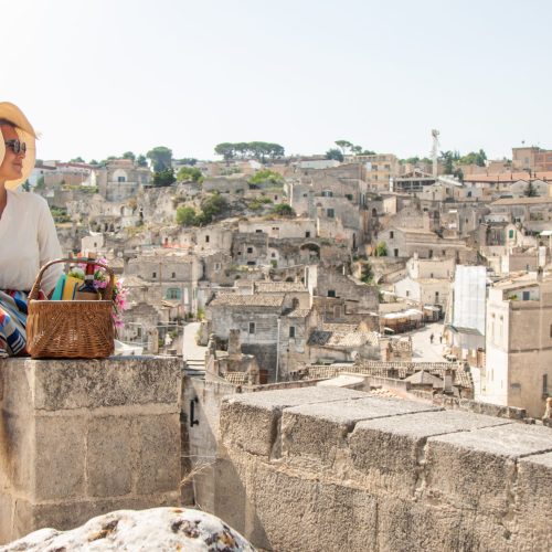 Young elegant woman tourist sitting in historical Matera town in Italy looking at city landscape
